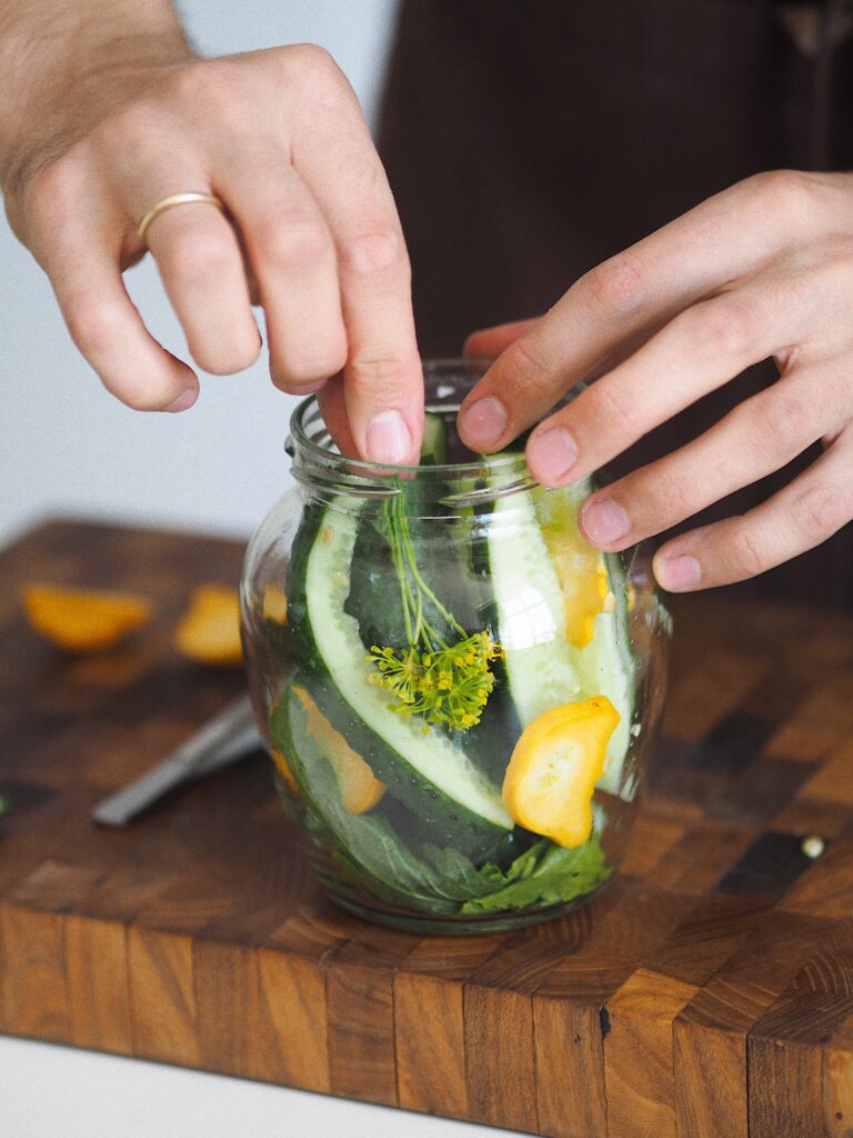 Pickling perfection: Hands filling a mason jar with cucumbers and pickling ingredients for a delicious homemade pickle batch.