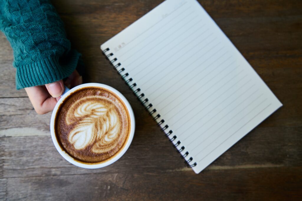 Person holding a latte and notepad, ready to jot down notes.