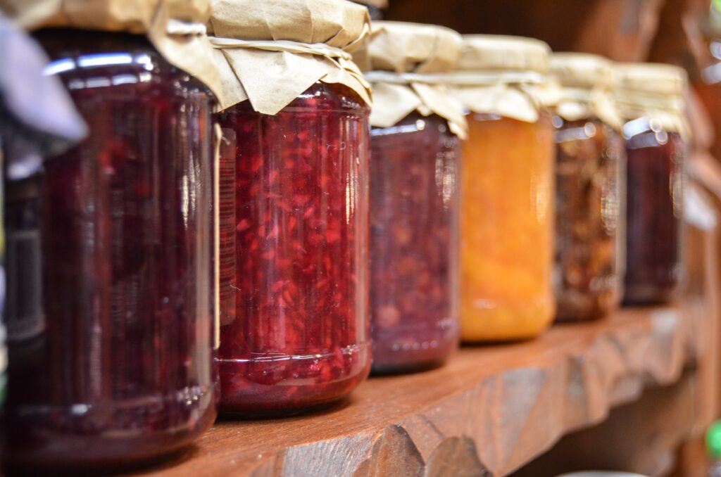 Preserving the harvest: Six mason jars filled with homemade jams and preserves, sealed with fabric and elastic bands.