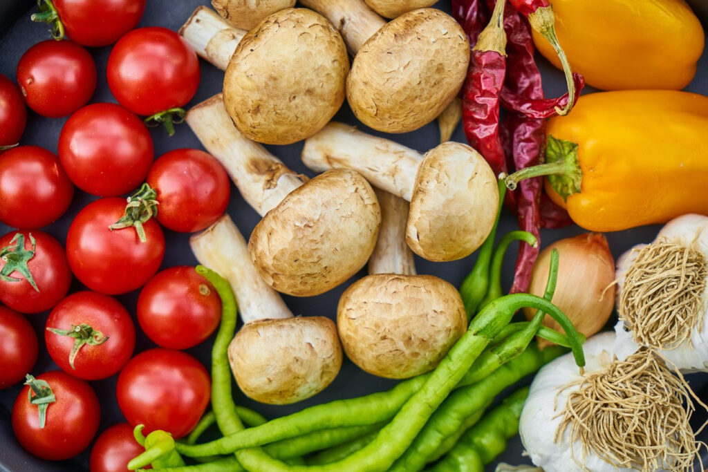 Assorted vegetables including cherry tomatoes, mushrooms, hot peppers, peppers, onions, and garlic on a cookie sheet.